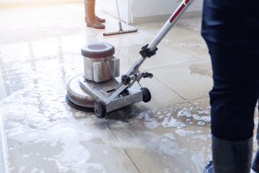 Here's an alt tag for the image: `Person cleaning floor with buffer machine`