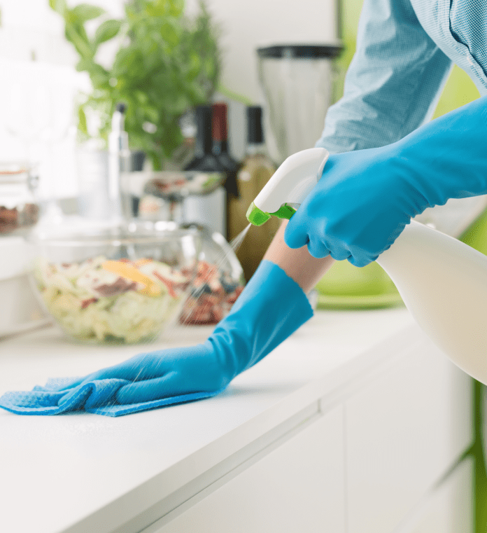 Person cleaning kitchen counter with spray bottle.